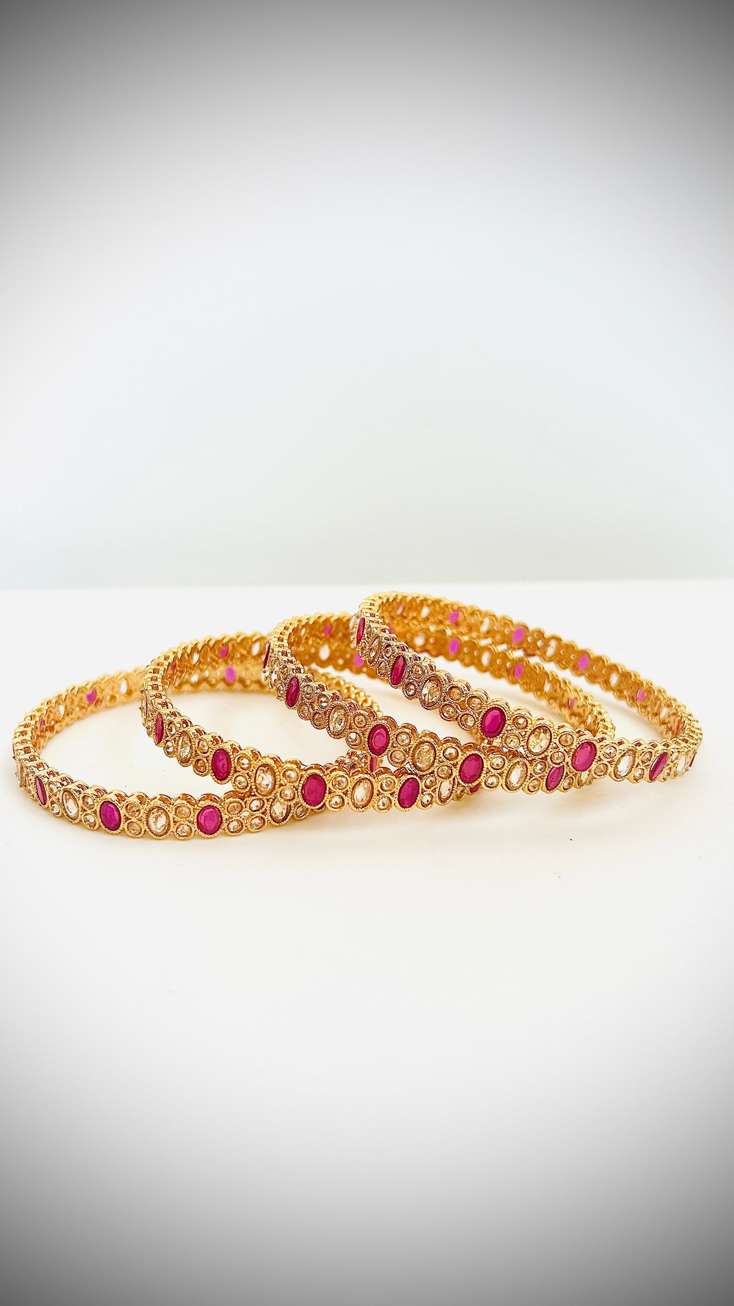 Set of 4 gold bangles with pink stones.