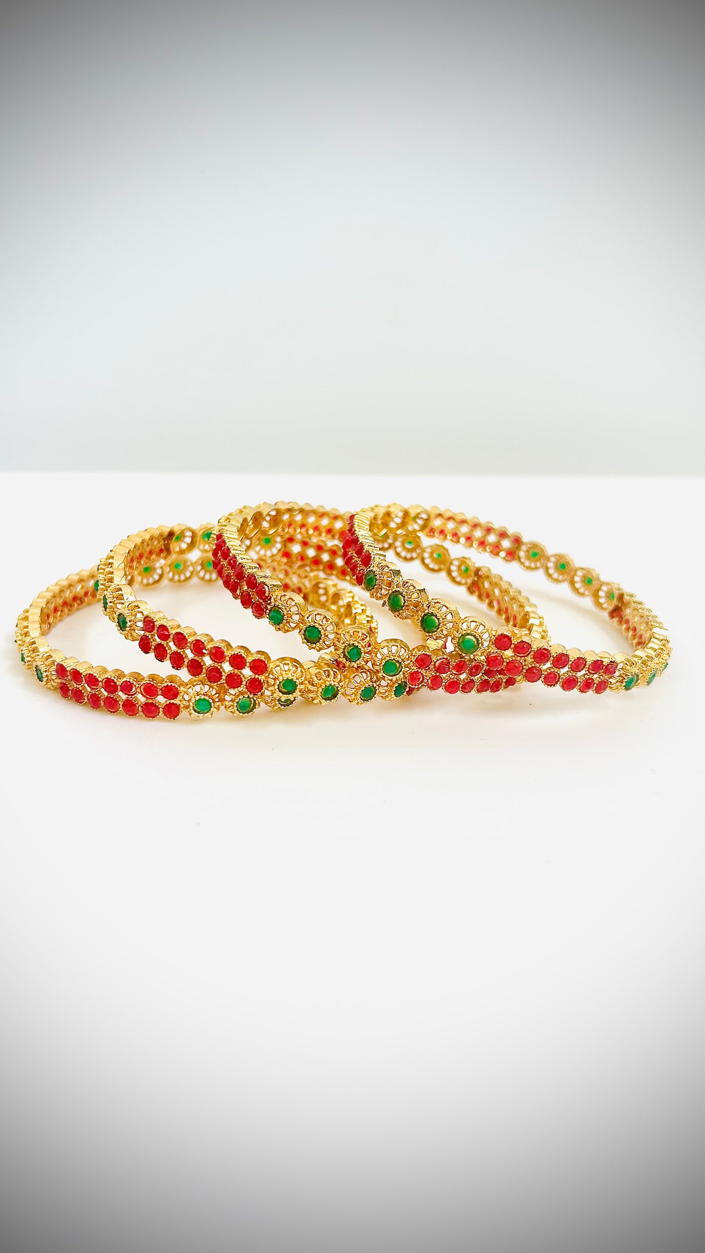 Set of gold bangles with red and green stones.
