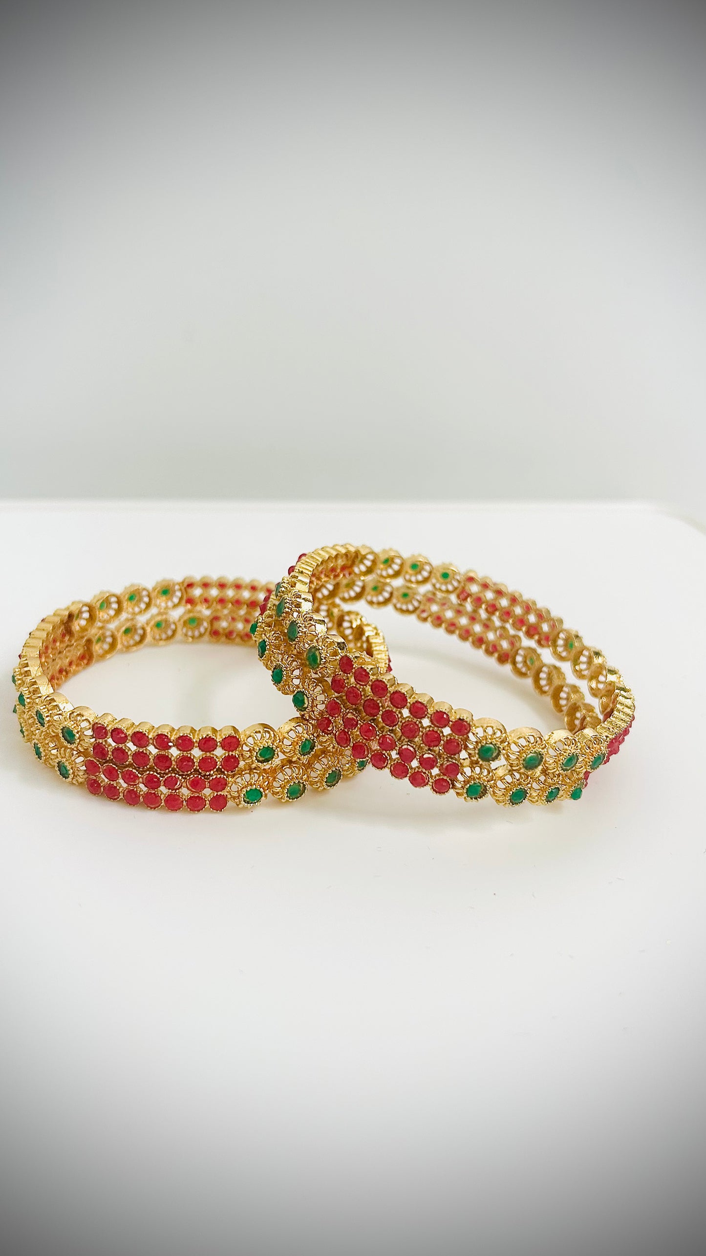 Pair of gold, green, and red beaded bracelets on a white surface with a gray background