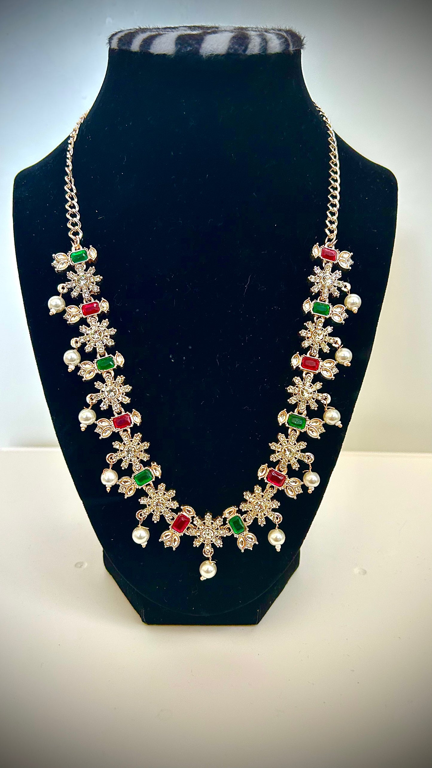 Necklace with floral designs and colored stones on a black stand.