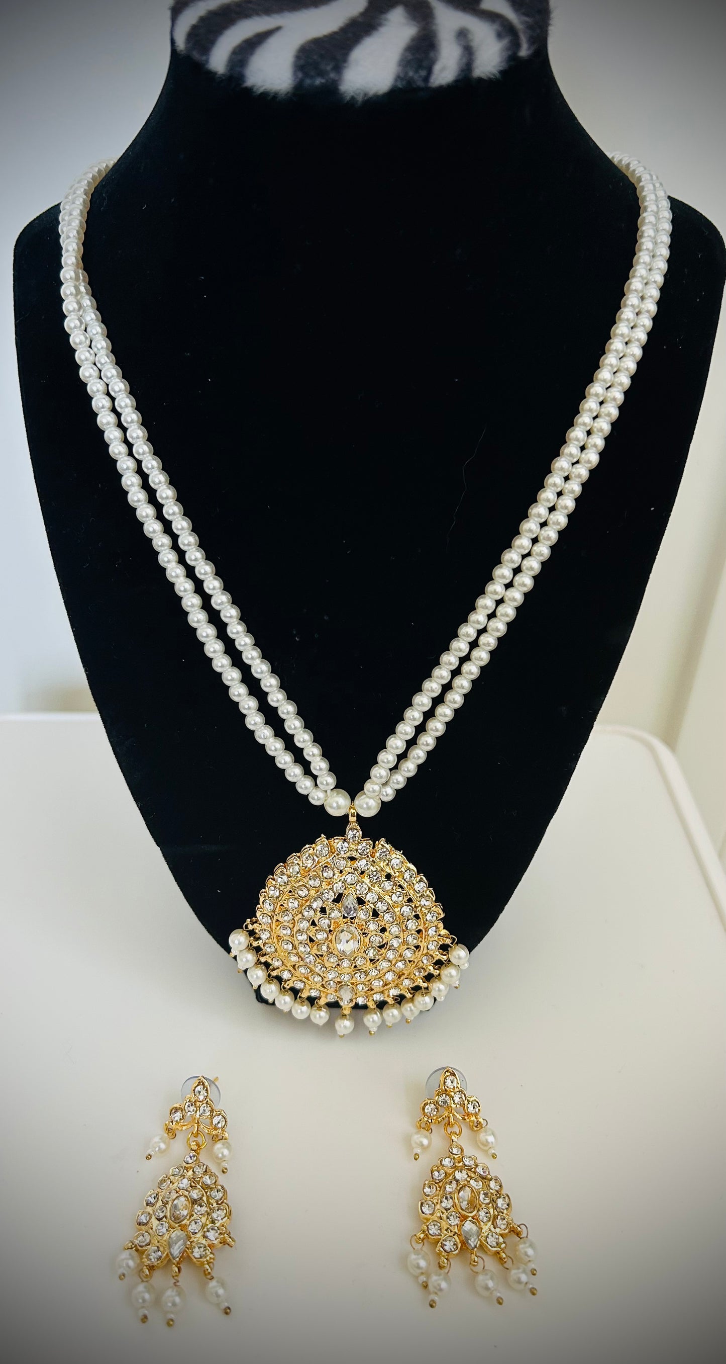 Pearl necklace with a gold pendant and matching earrings on a black mannequin bust.