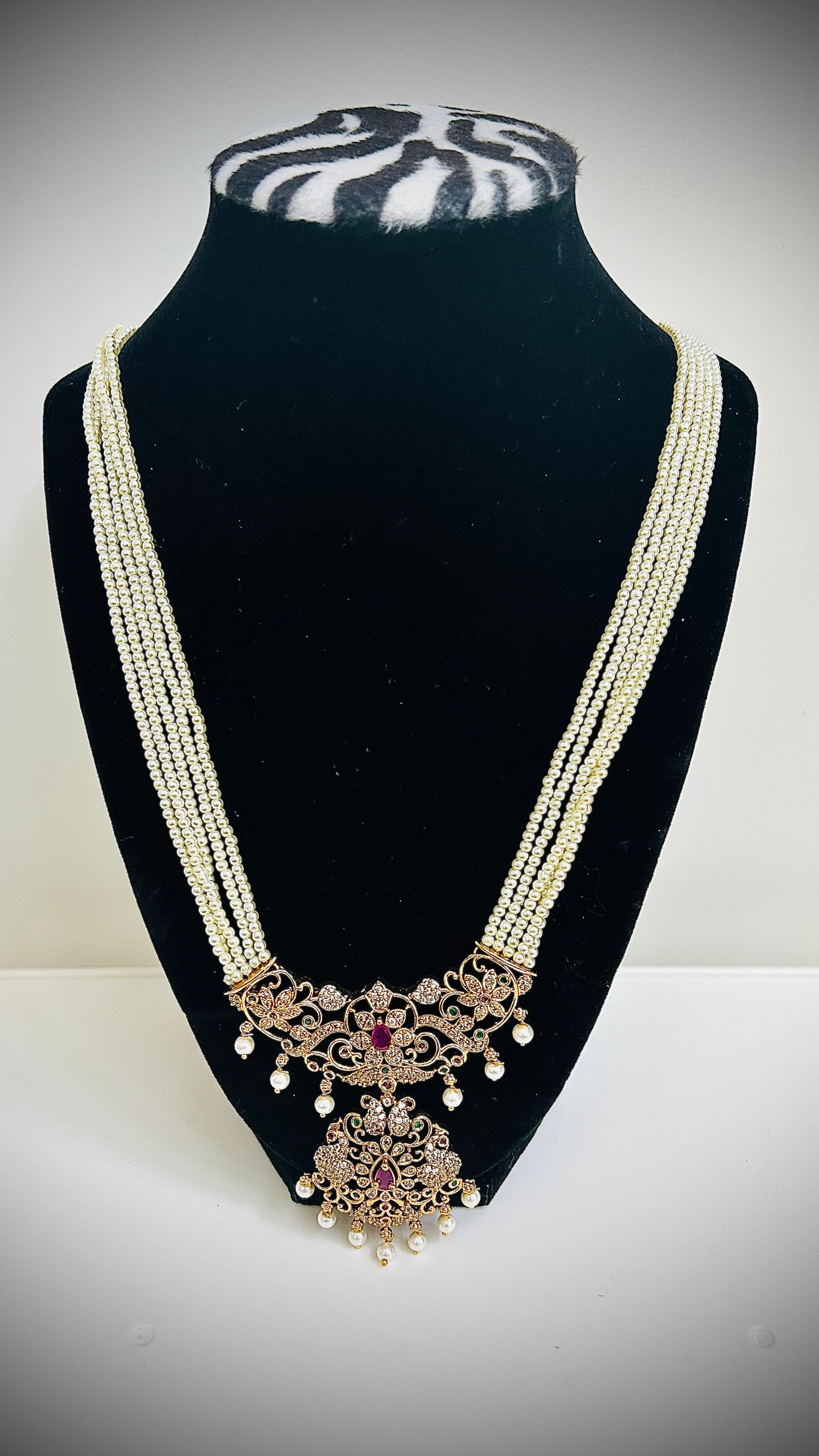 Delicate necklace with intricate design on a black stand against a white background