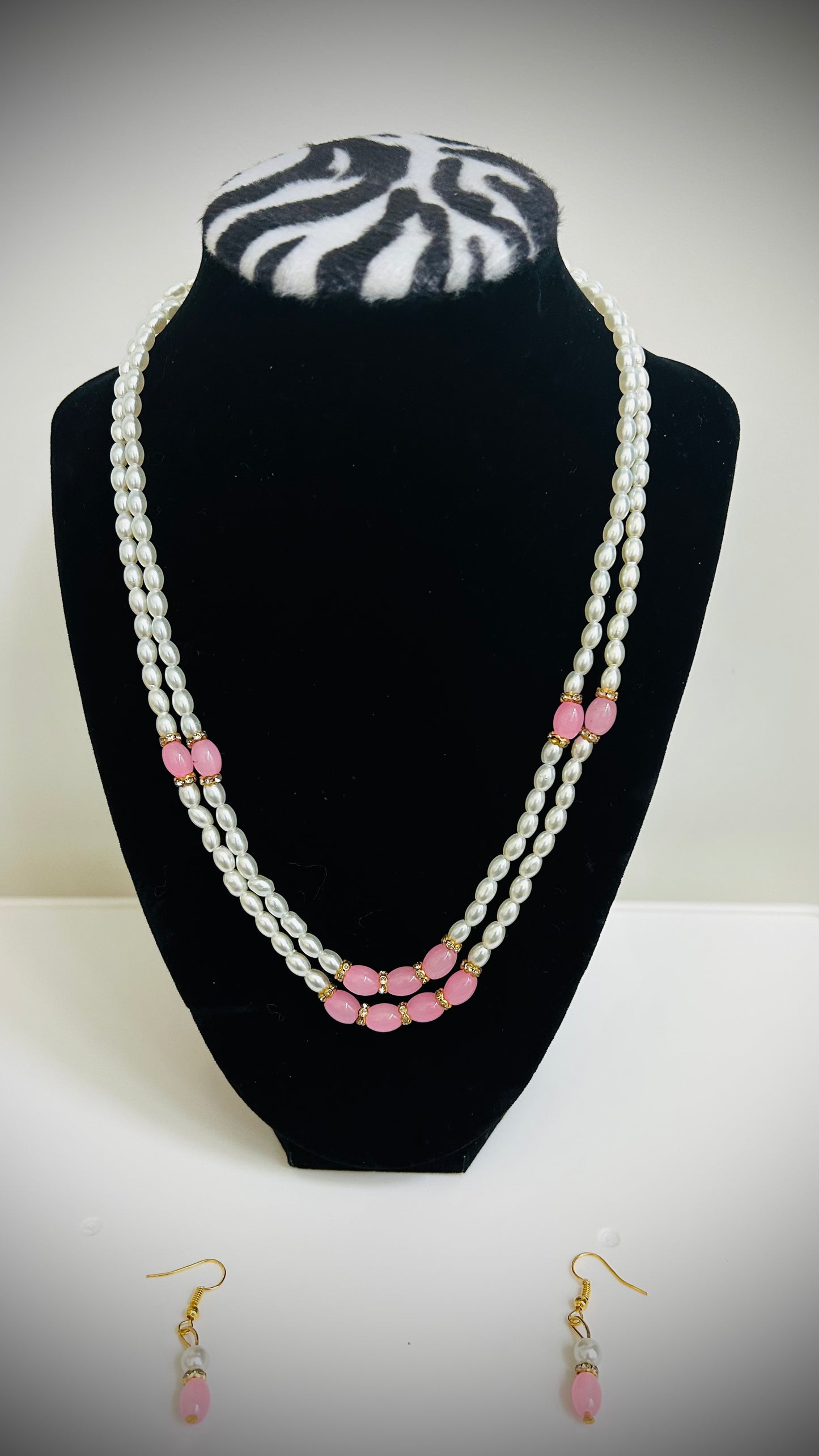 Pearl necklace with pink beads on a black stand, accompanied by matching earrings.