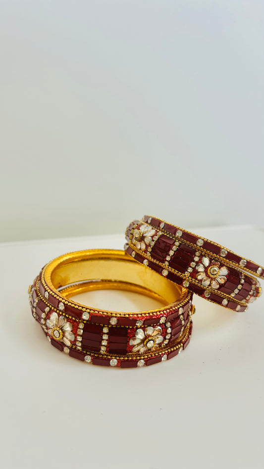 Two ornate bangles with maroon and gold design on a white background