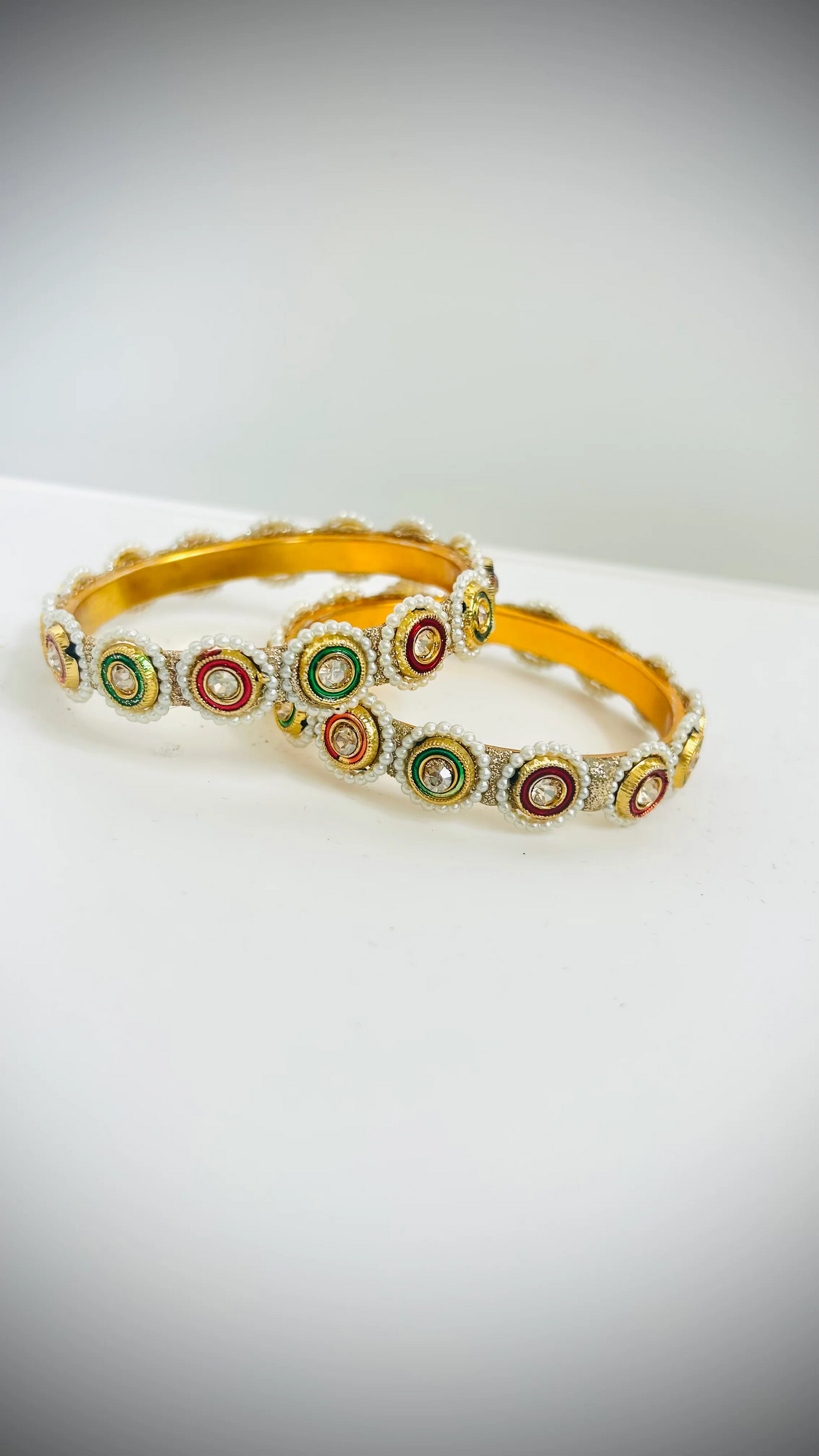 Pair of gold bangles decorated with green and red stones set on white circles.