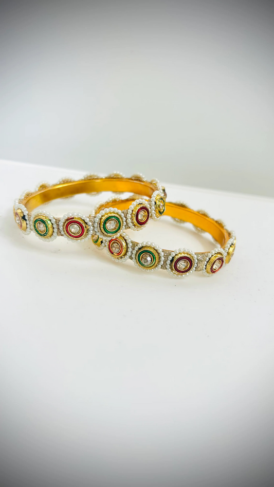 Pair of gold bangles decorated with green and red stones set on white circles.