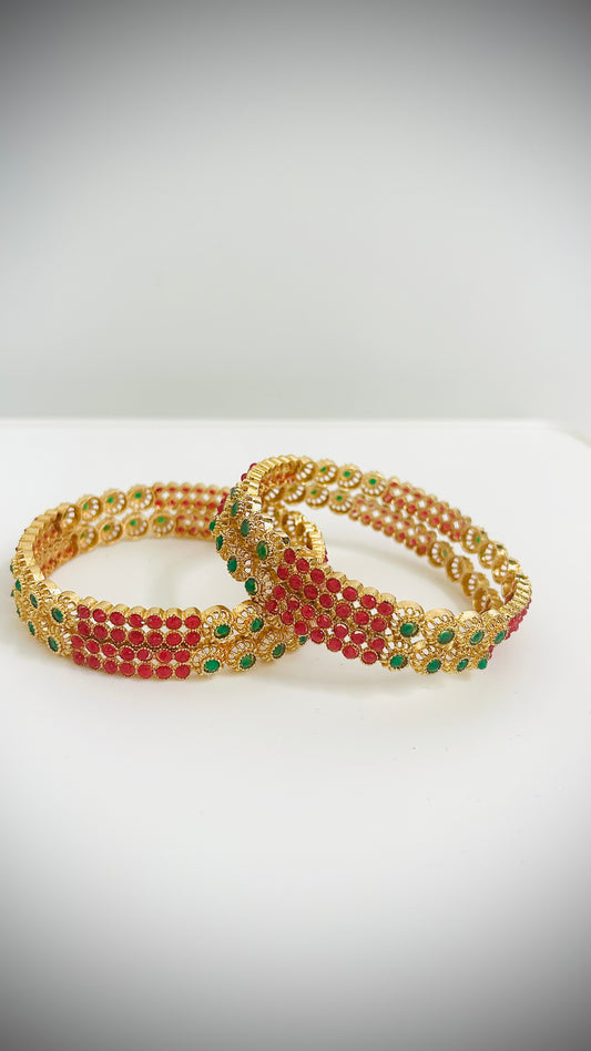 Pair of gold, green, and red beaded bracelets on a white surface with a gray background