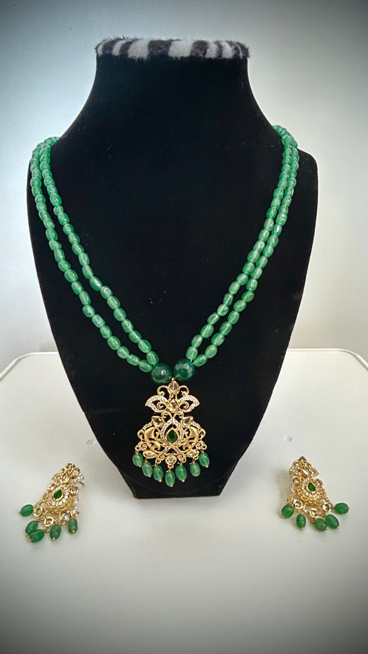 Green beaded necklace with gold pendant and matching earrings on a black mannequin bust.