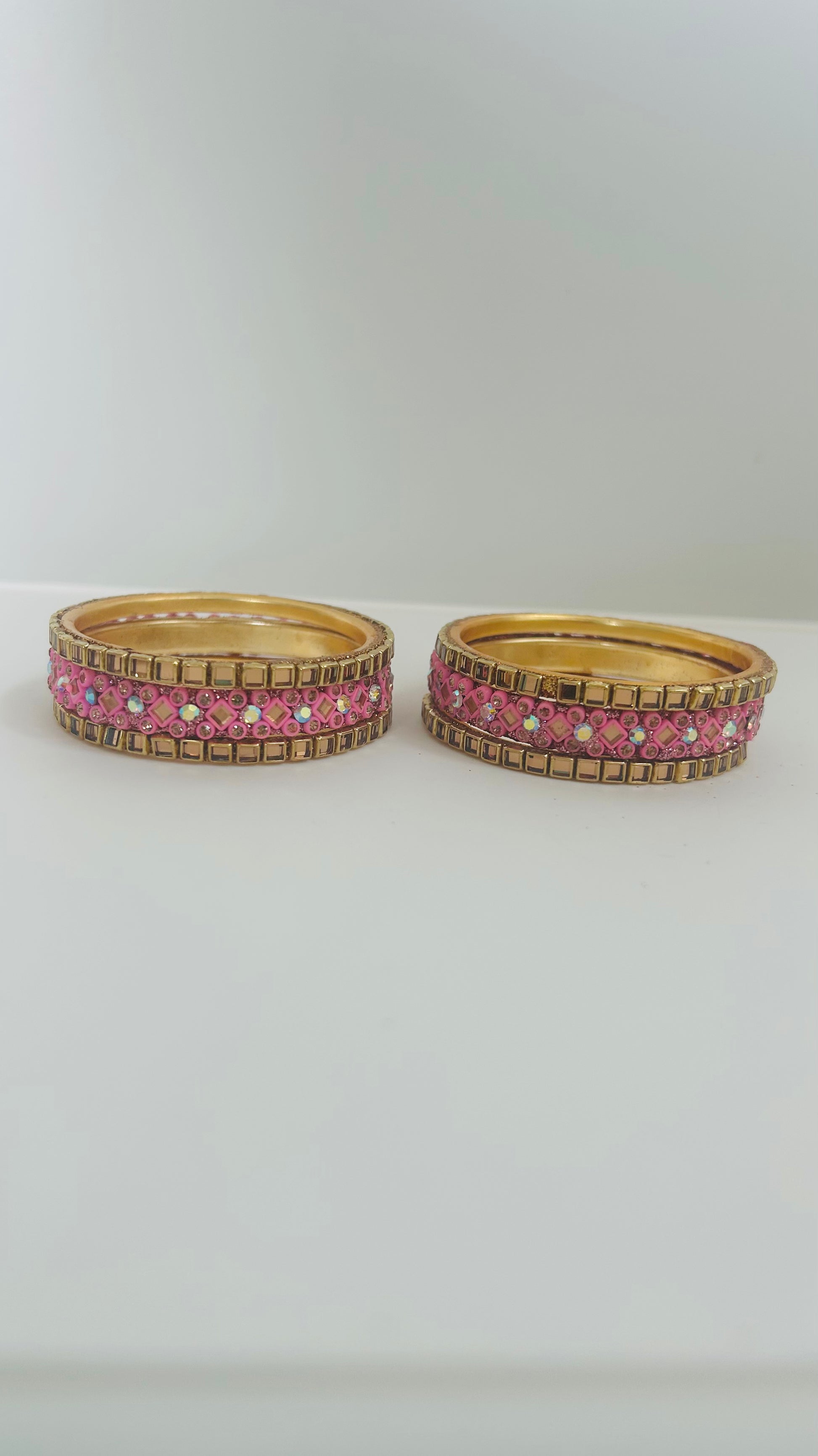 Two gold bangles with pink gemstones on a white background