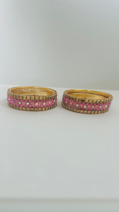 Two gold bangles with pink gemstones on a white background